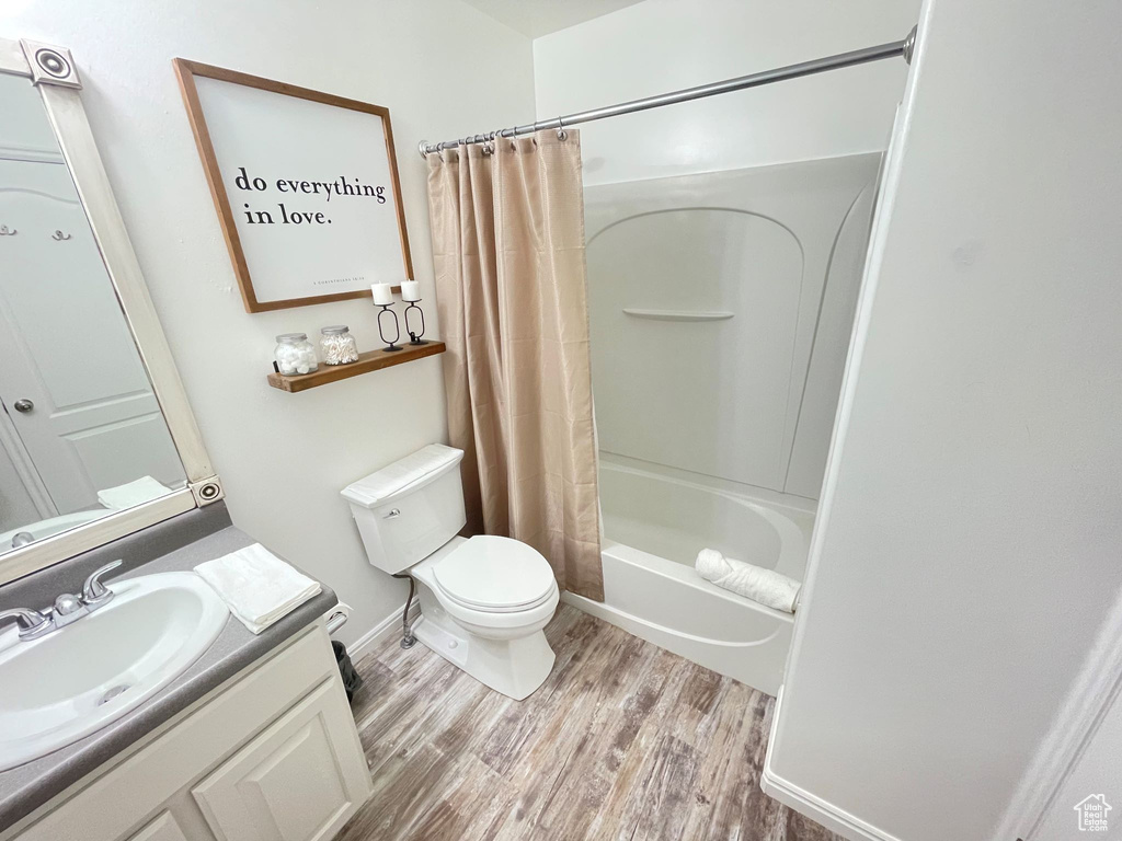 Full bathroom featuring shower / tub combo with curtain, toilet, vanity, wood finished floors, and baseboards