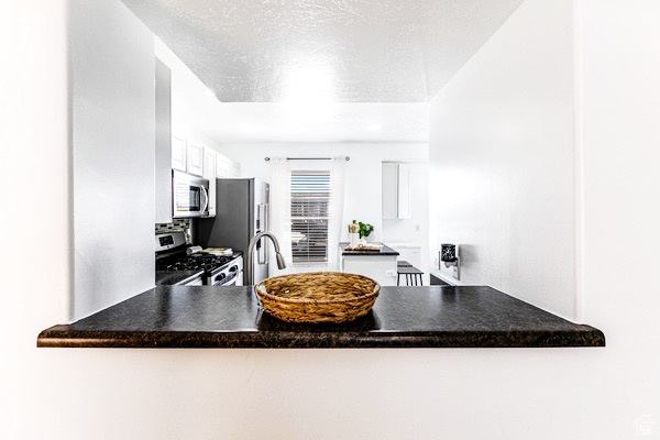 Kitchen featuring a textured ceiling, stainless steel appliances, a peninsula, white cabinetry, and dark countertops