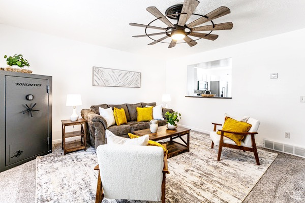 Living room featuring a ceiling fan, visible vents, carpet floors, and baseboards