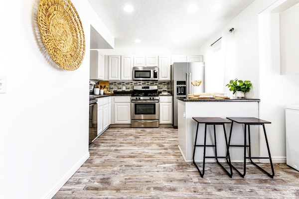 Kitchen with dark countertops, light wood finished floors, appliances with stainless steel finishes, and backsplash