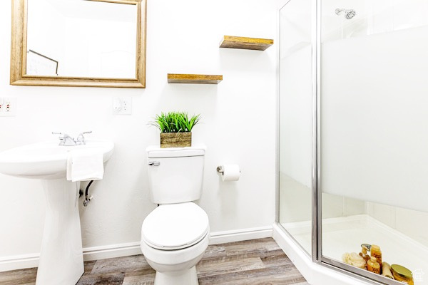 Bathroom with baseboards, a shower stall, toilet, and wood finished floors