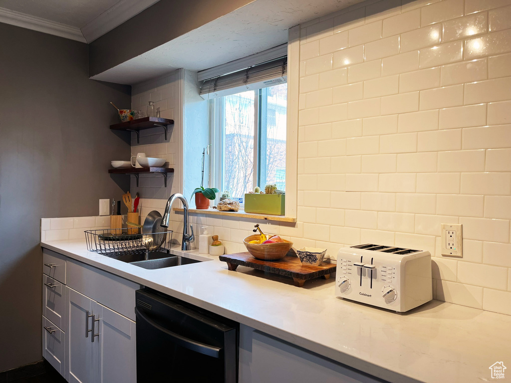 Kitchen featuring black dishwasher, a sink, ornamental molding, light countertops, and backsplash