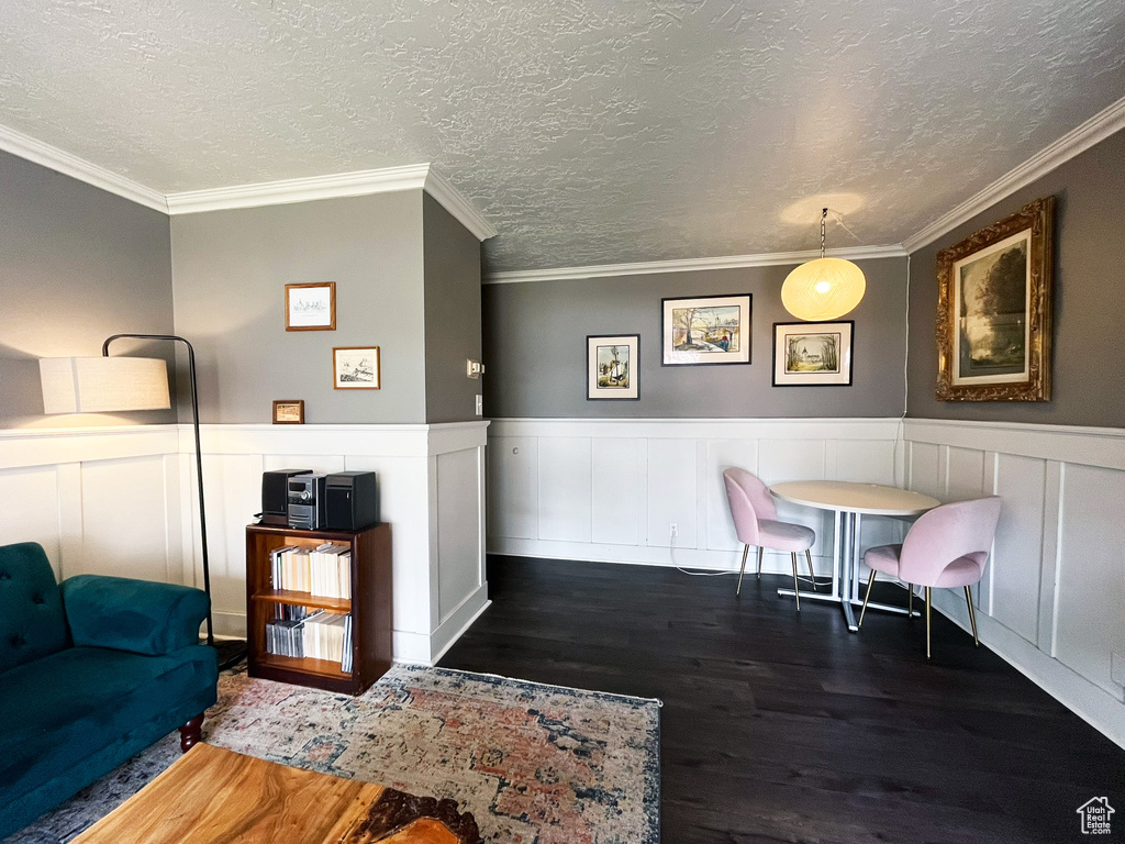 Dining area featuring wood finished floors, a textured ceiling, a decorative wall, and ornamental molding