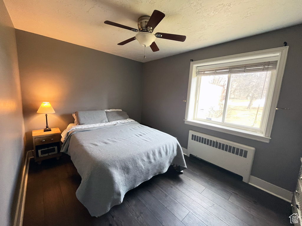 Bedroom featuring radiator, dark wood-style flooring, baseboards, and a ceiling fan
