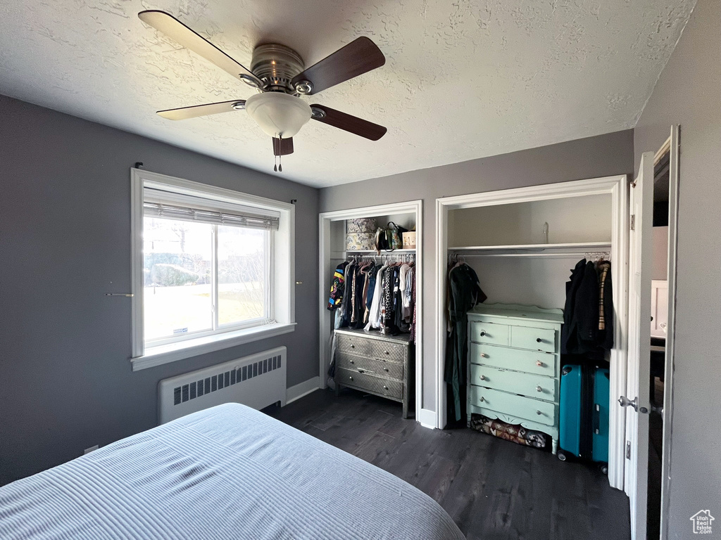 Bedroom with radiator, two closets, dark wood-type flooring, a textured ceiling, and ceiling fan