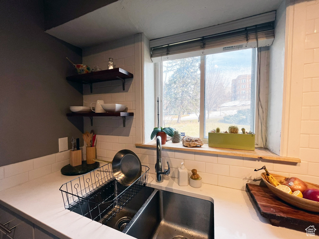 Kitchen view of decorative backsplash, light countertops, a sink, and open shelves