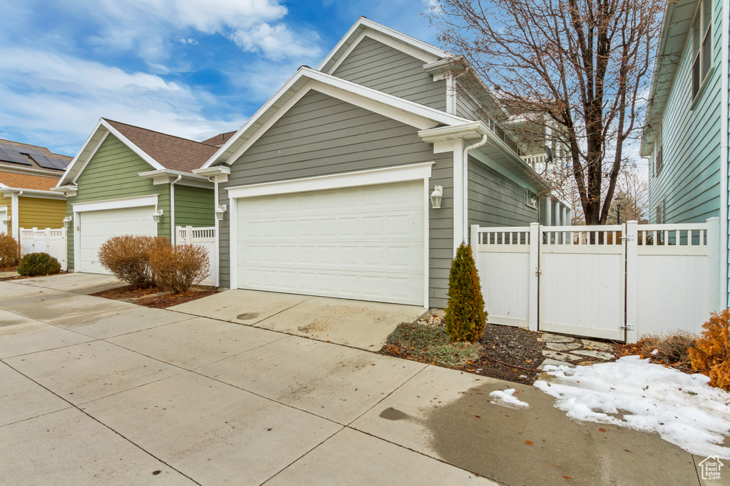 View of front of property featuring a garage, concrete driveway, fence, and a gate