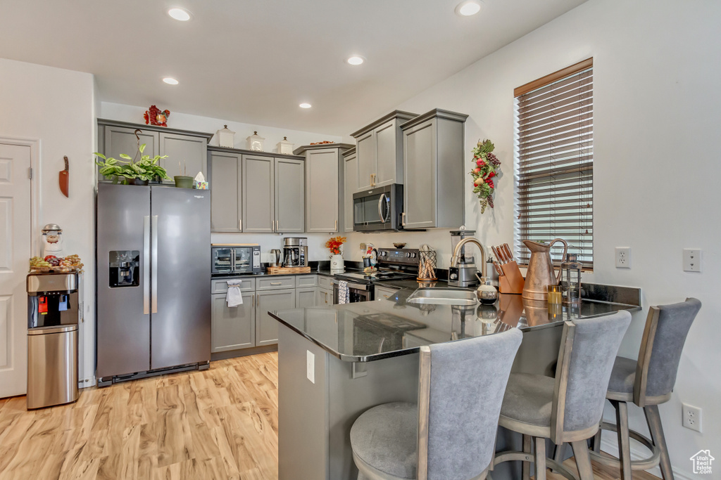 Kitchen with gray cabinets, appliances with stainless steel finishes, a sink, light wood-type flooring, and a peninsula