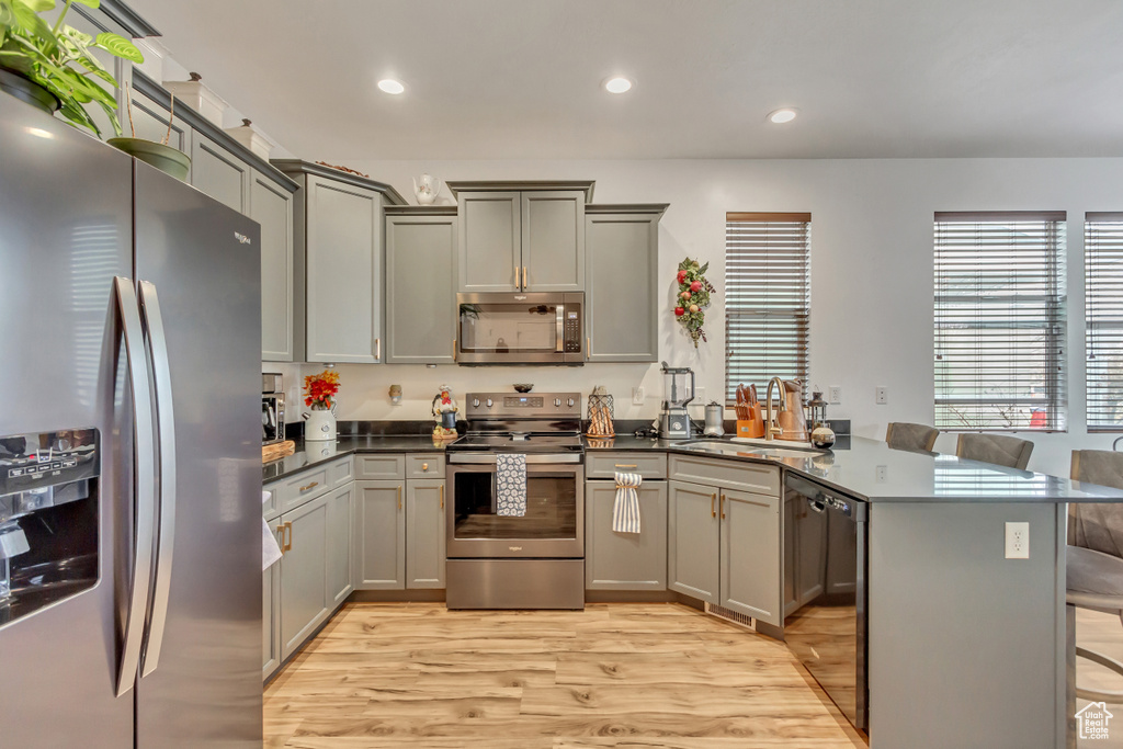Kitchen with light wood-style flooring, appliances with stainless steel finishes, a sink, a peninsula, and a kitchen bar