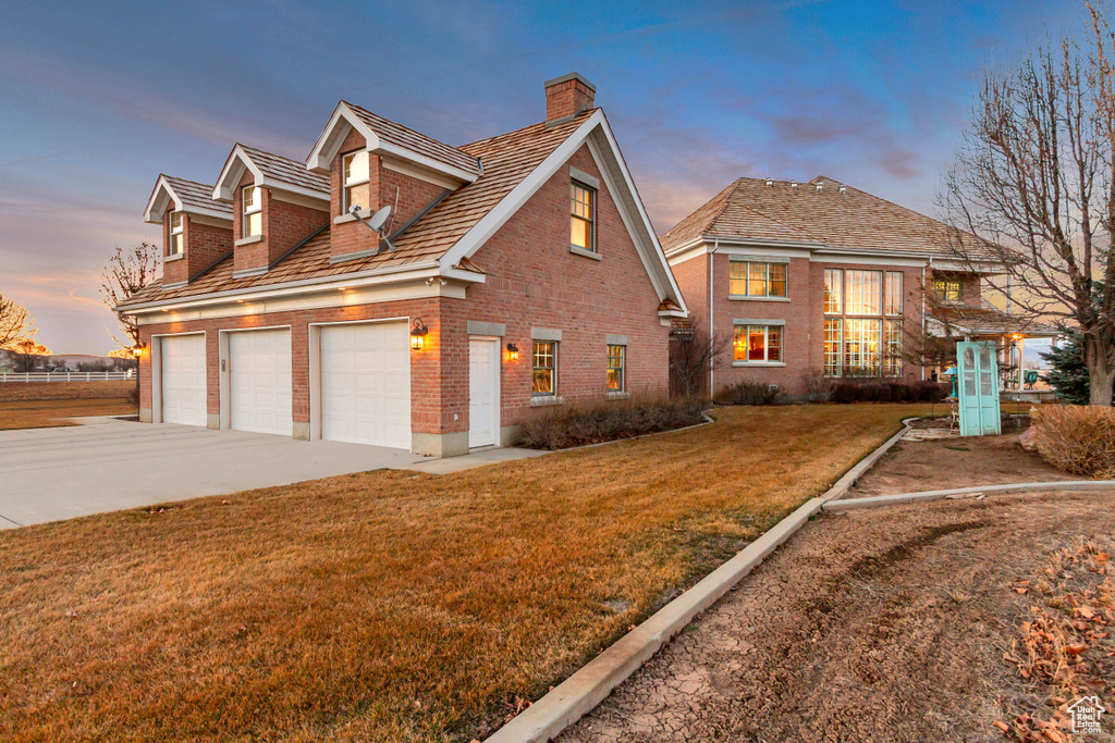 View of front of property featuring brick siding, a yard, a chimney, a garage, and driveway