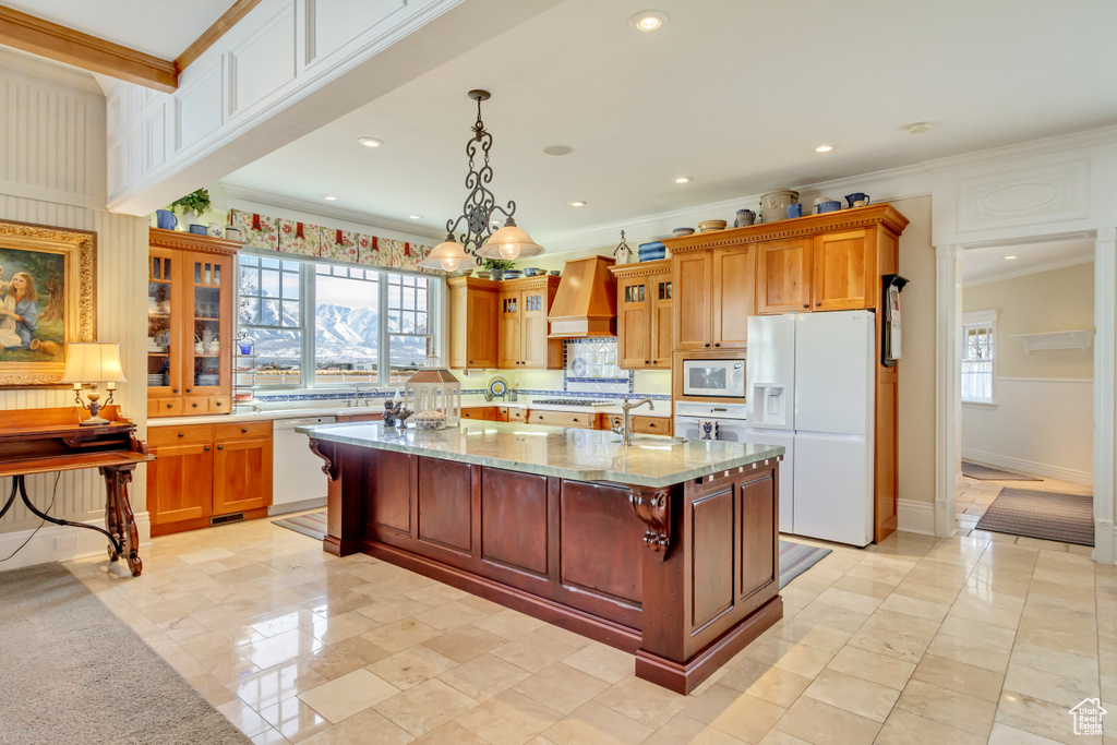 Kitchen featuring white appliances, custom exhaust hood, glass insert cabinets, and a healthy amount of sunlight