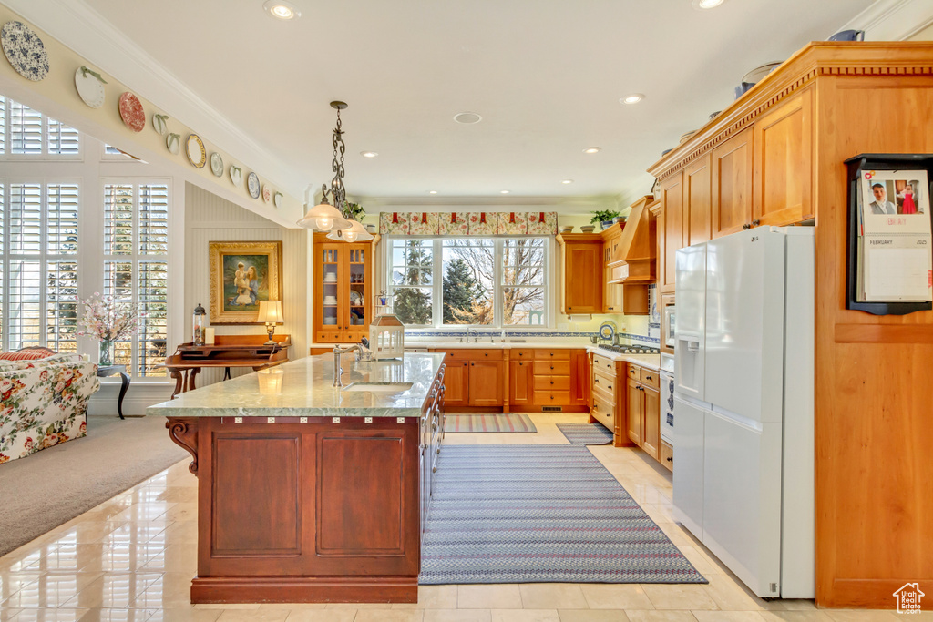 Kitchen featuring white appliances, custom range hood, a kitchen island with sink, crown molding, and a sink