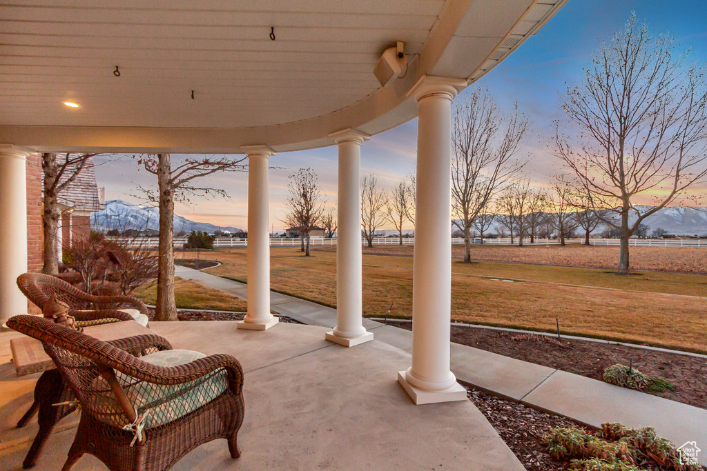 Patio terrace at dusk with covered porch, a lawn, and a mountain view