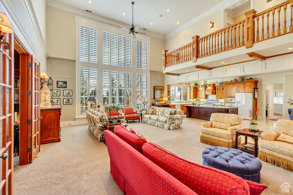 Living room with light carpet, ornamental molding, a towering ceiling, and a ceiling fan