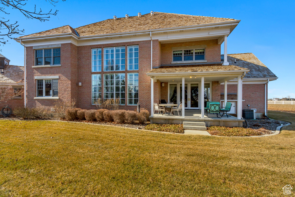 Rear view of house with a yard, french doors, brick siding, and central AC unit