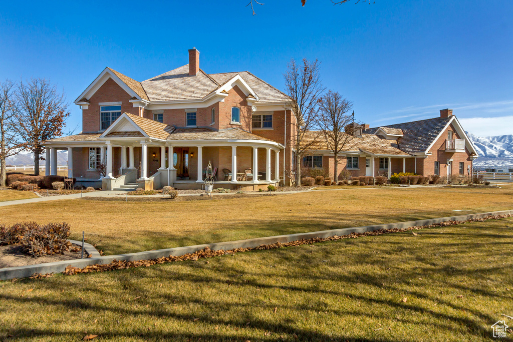 View of front of house with covered porch, brick siding, a chimney, and a front lawn