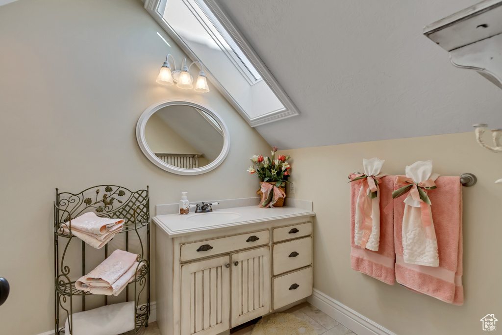 Bathroom with lofted ceiling with skylight, tile patterned flooring, vanity, and baseboards