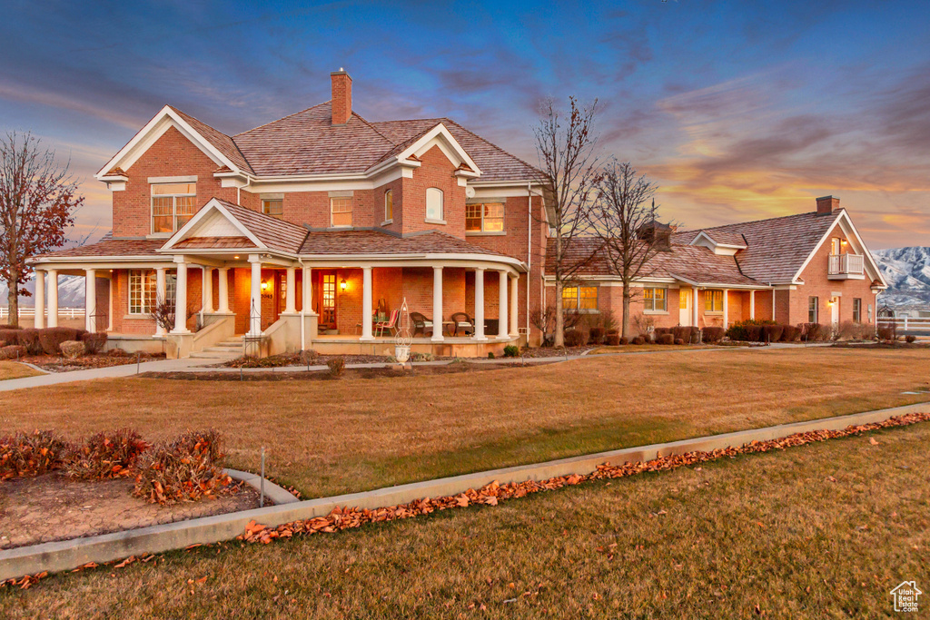 View of front of house with covered porch, brick siding, a yard, and a chimney