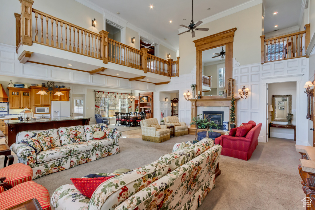 Living room with light carpet, a tiled fireplace, ornamental molding, a high ceiling, and a decorative wall