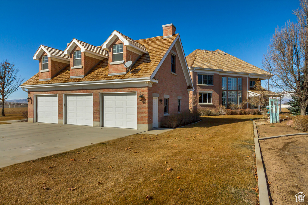 View of front of home with driveway, a garage, a chimney, a front lawn, and brick siding