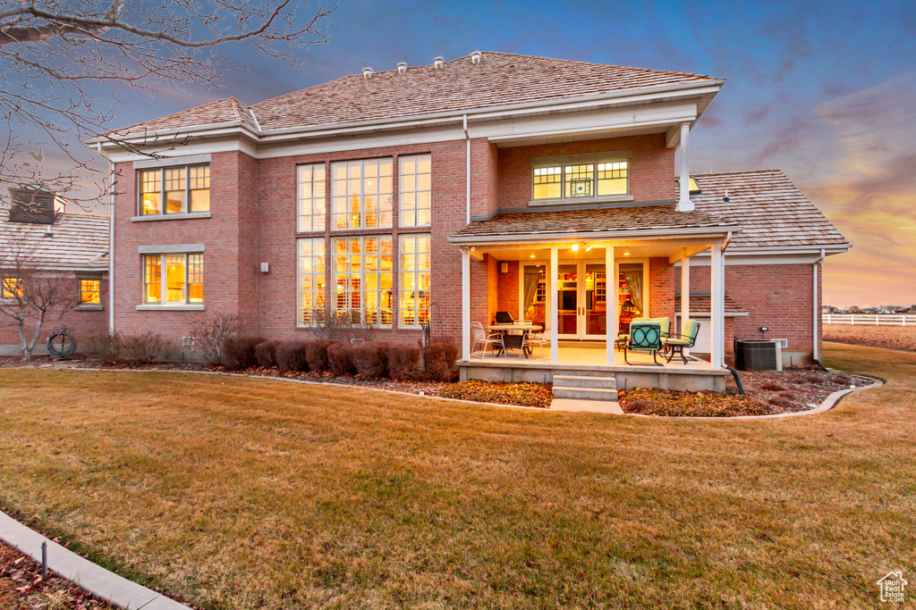 Back of house at dusk featuring a yard, brick siding, french doors, and central air condition unit