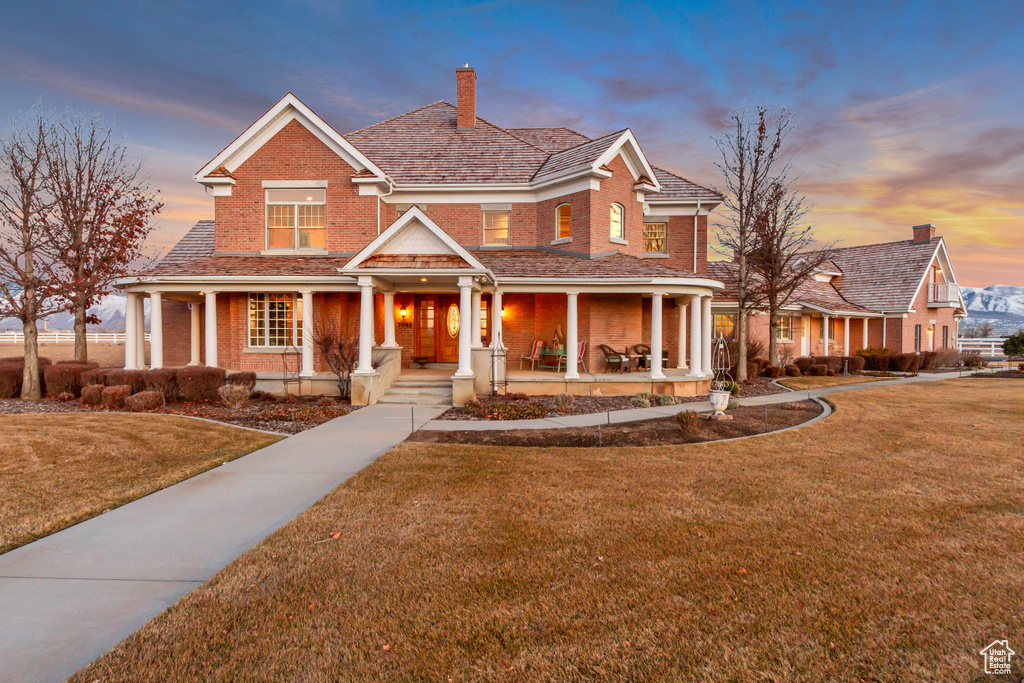 View of front of home with covered porch, brick siding, a chimney, and a front yard