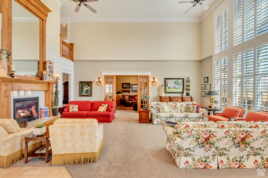 Living area with carpet floors, a glass covered fireplace, a ceiling fan, and crown molding