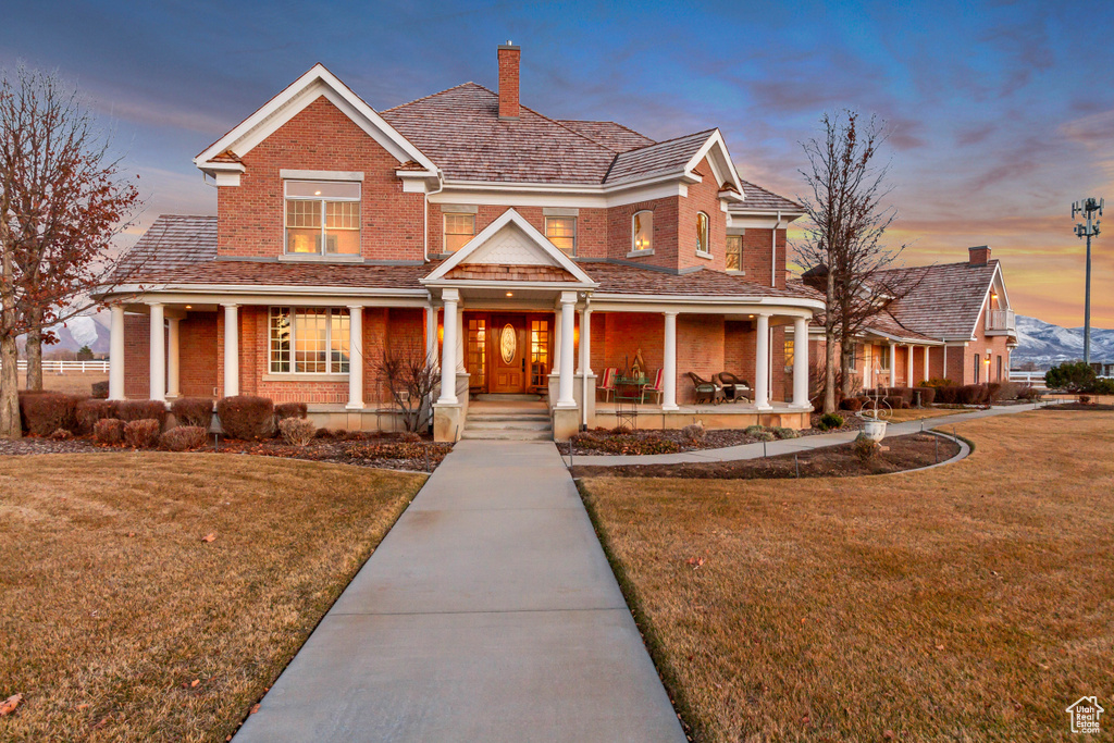 View of front of property featuring a yard, brick siding, a chimney, and a porch