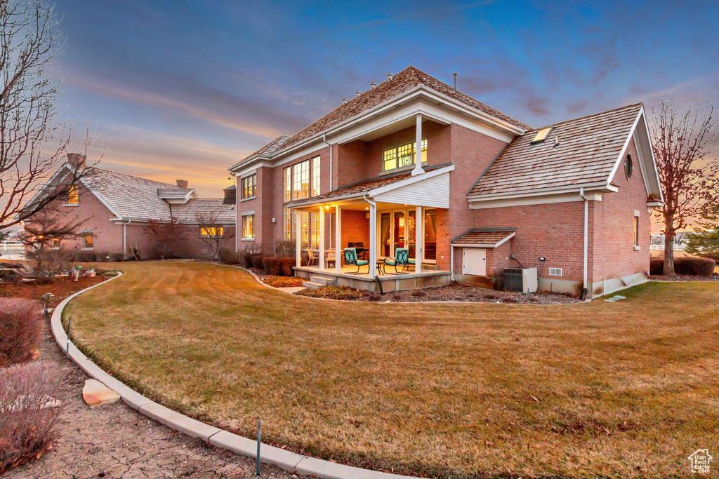 Back of property at dusk featuring a yard, central AC, and brick siding