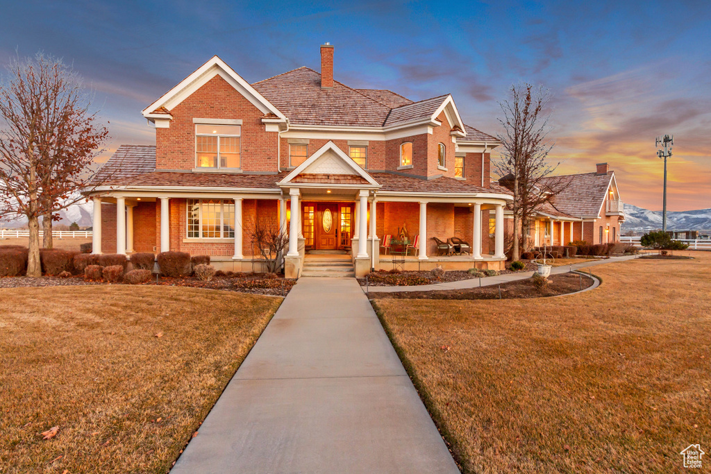 View of front of home featuring a porch, a front yard, brick siding, and a chimney