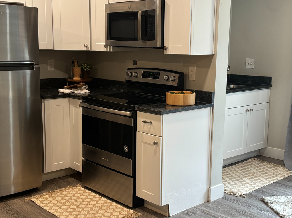 Kitchen featuring stainless steel appliances, dark wood-style floors, dark countertops, white cabinets, and recessed lighting