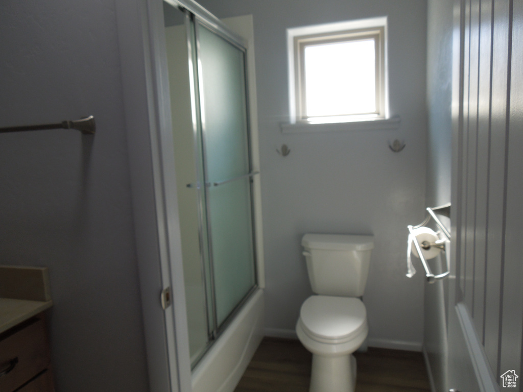 Full bathroom featuring toilet, combined bath / shower with glass door, vanity, wood finished floors, and baseboards