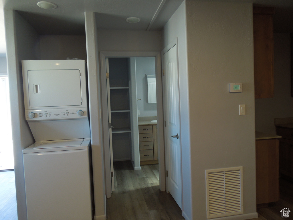 Laundry room featuring laundry area, stacked washing maching and dryer, wood finished floors, and visible vents