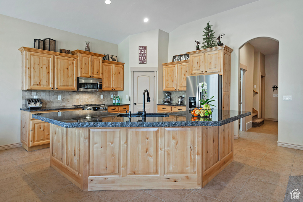 Kitchen with appliances with stainless steel finishes, light brown cabinets, and a center island with sink