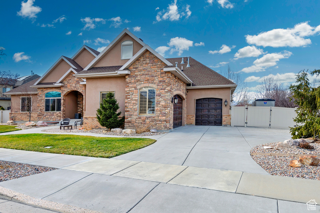 View of front facade featuring driveway, an attached garage, a gate, and stucco siding