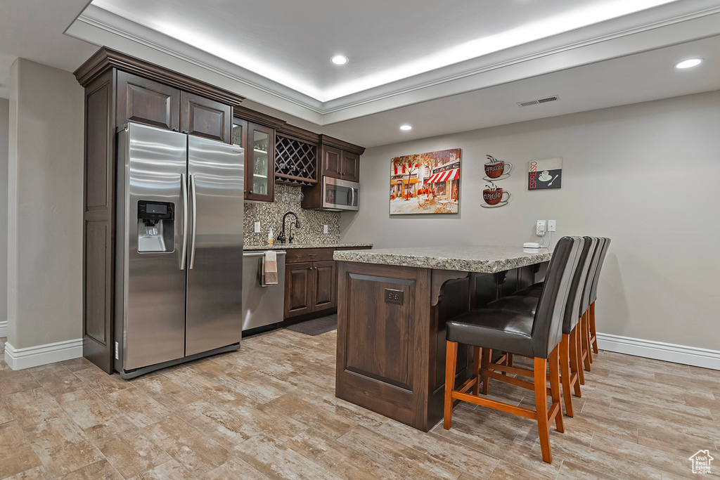 Kitchen featuring stainless steel appliances, light countertops, glass insert cabinets, dark brown cabinetry, and a kitchen breakfast bar