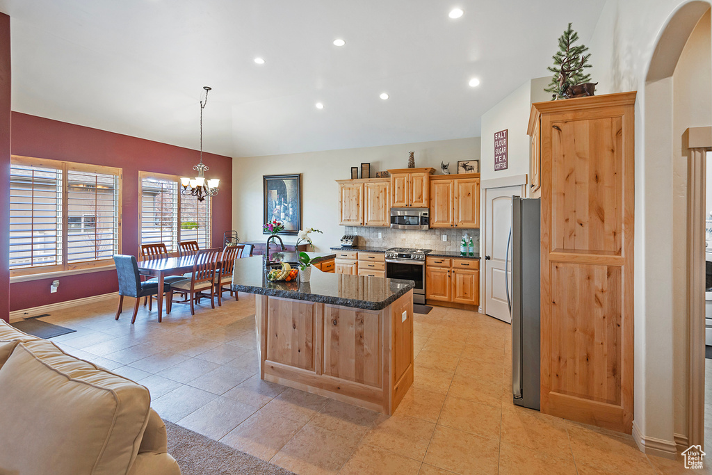 Kitchen featuring pendant lighting, lofted ceiling, appliances with stainless steel finishes, open floor plan, and a kitchen island with sink