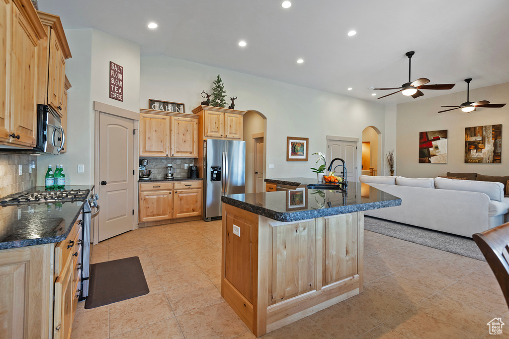 Kitchen featuring arched walkways, appliances with stainless steel finishes, open floor plan, a kitchen island with sink, and light brown cabinets