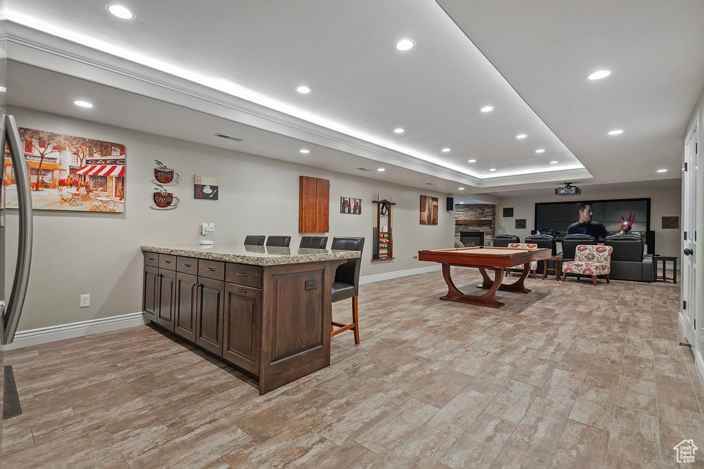 Rec room featuring visible vents, baseboards, a tray ceiling, a stone fireplace, and recessed lighting