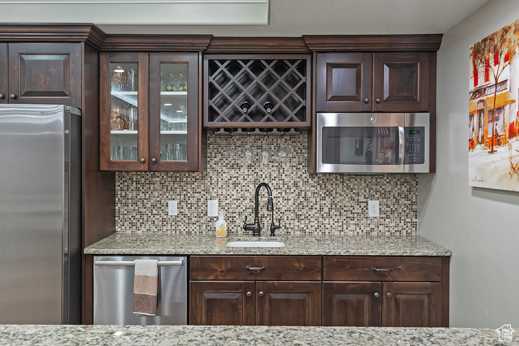 Bar featuring appliances with stainless steel finishes, indoor wet bar, a sink, and tasteful backsplash