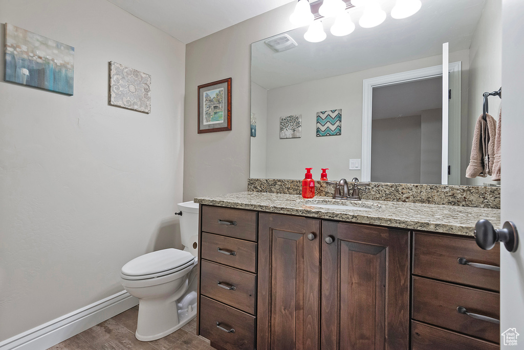 Bathroom featuring baseboards, visible vents, toilet, wood finished floors, and vanity