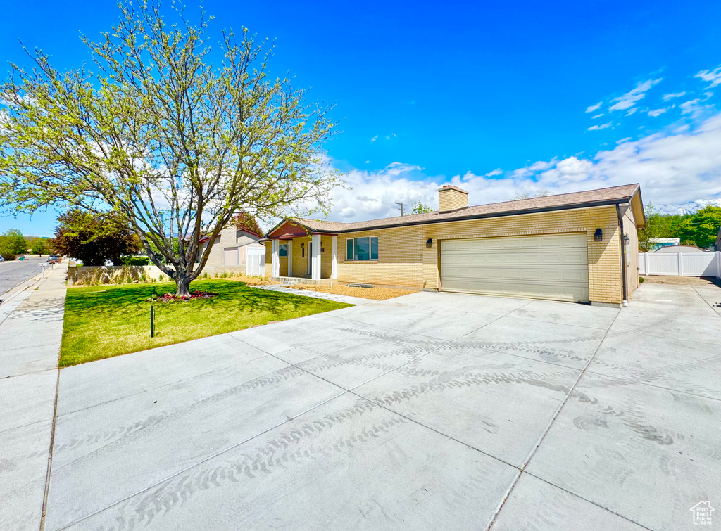 Single story home featuring an attached garage, brick siding, a front yard, a chimney, and concrete driveway
