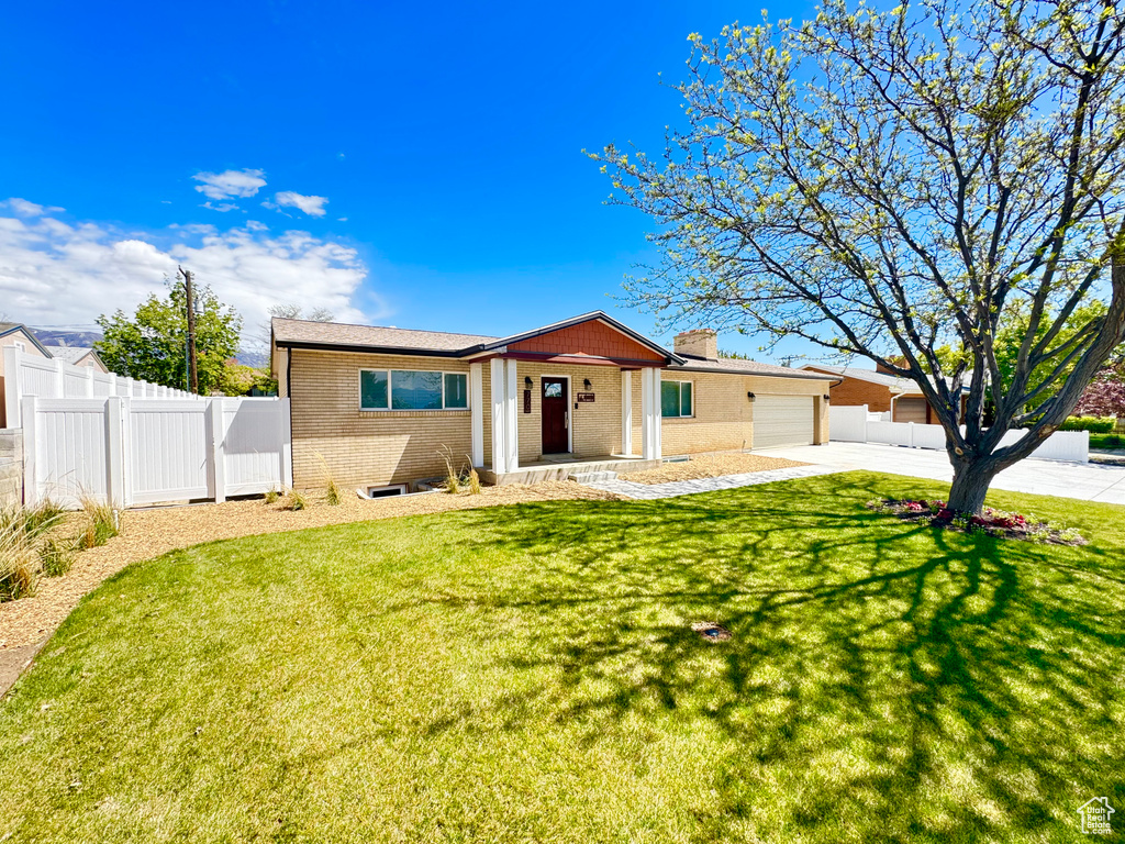 Ranch-style house with driveway, a front yard, brick siding, fence, and an attached garage