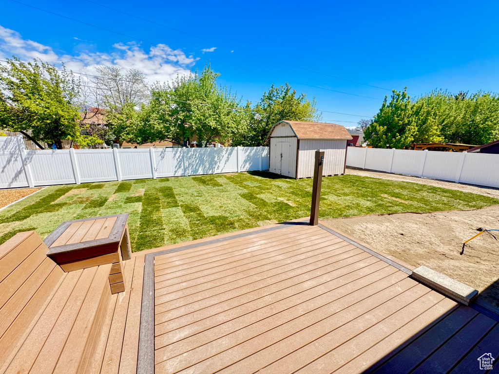 Wooden deck featuring a storage shed, a lawn, an outbuilding, and a fenced backyard