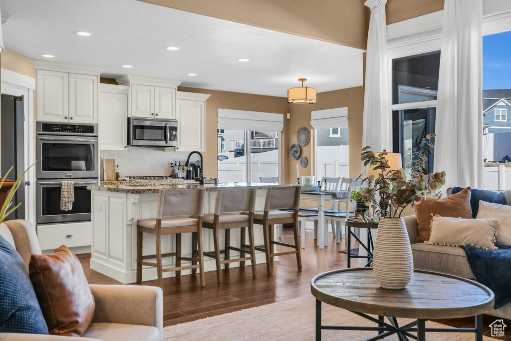 Kitchen with stainless steel appliances, tasteful backsplash, dark stone countertops, wood finished floors, and a kitchen bar