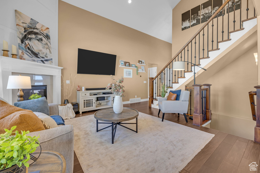 Living room featuring wood finished floors, visible vents, a towering ceiling, stairway, and a glass covered fireplace