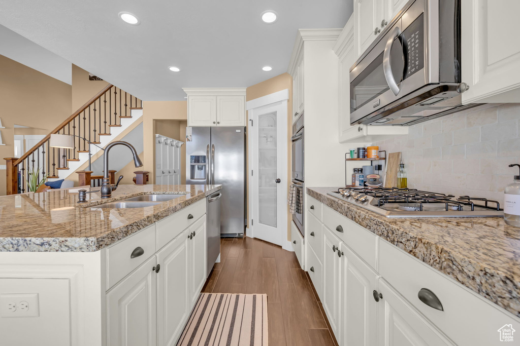 Kitchen with light stone counters, a sink, white cabinetry, appliances with stainless steel finishes, and dark wood finished floors