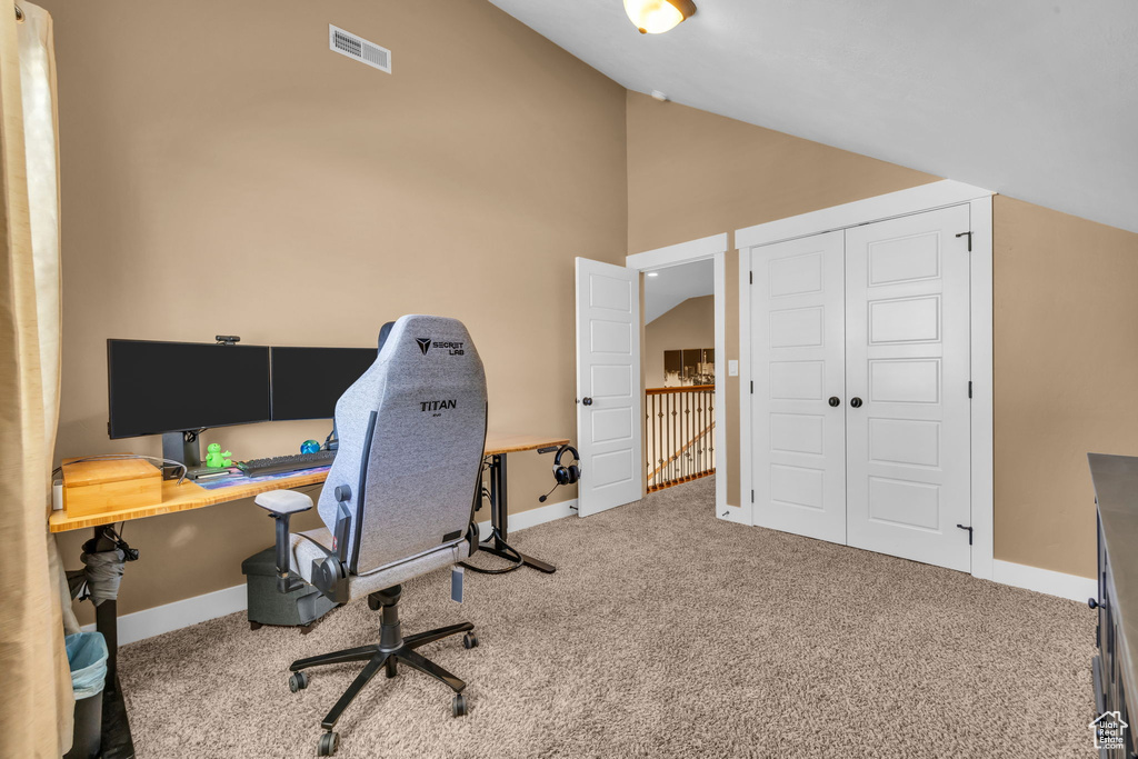 Carpeted home office with lofted ceiling, visible vents, and baseboards