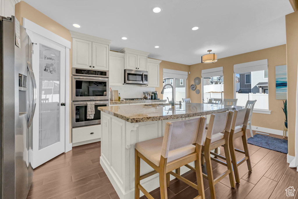 Kitchen with stainless steel appliances, a sink, light stone countertops, and wood tiled floor