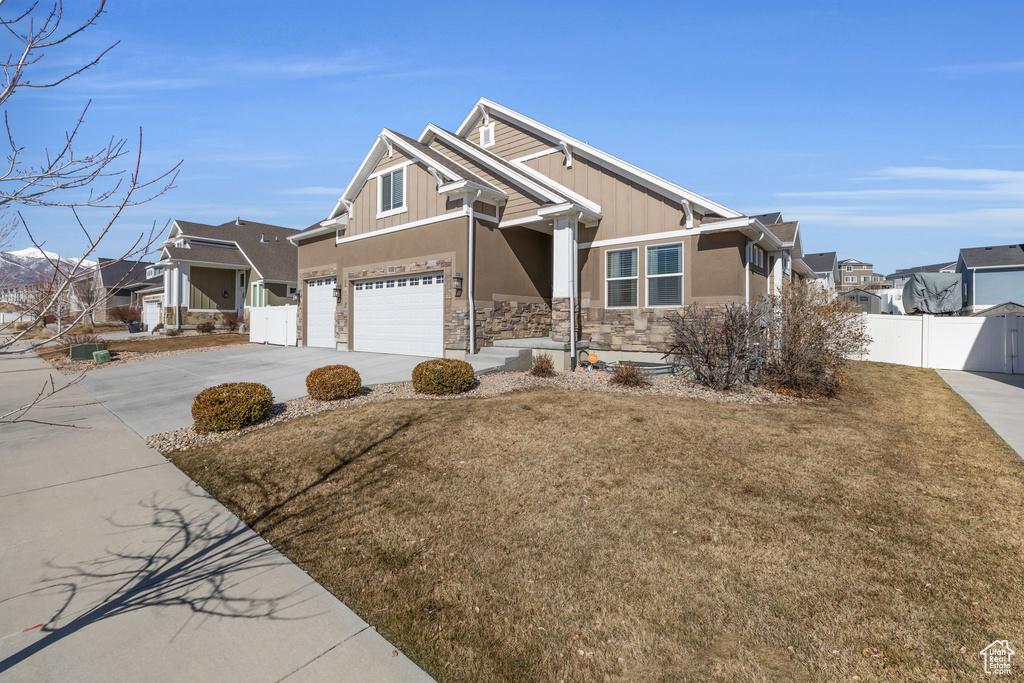 Craftsman house with concrete driveway, stone siding, a residential view, fence, and board and batten siding